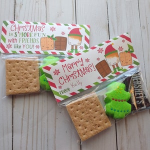May include: Two clear plastic bags filled with ingredients for making s'mores. The bags are decorated with Christmas-themed labels featuring a cartoon elf and the text "Christmas is S'more Fun with Friends like YOU!" and "Merry Christmas! From: Kelly".