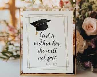 May include: A framed print with a gold border features a graduation cap illustration and the text "God is within her, she will not fall" from Psalm 46:5. The print is set against a blurred floral background.