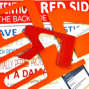 Puede incluir: Primer plano de varias plantillas de papel naranja y rojo con el texto "RED SIDE" y "ATTENTION THE BACK" visible. Las plantillas están dispuestas una encima de la otra, creando un efecto de capas.