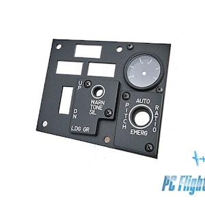 Może przedstawiać: Czarny metalowy panel z różnymi przełącznikami i okrągłym wskaźnikiem. Panel zawiera etykiety takie jak "Warn Tone Sil", "Pitch Emerg", "Auto Ratio" i "Ldg Gr".