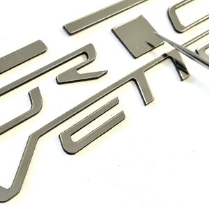 May include: Close-up of a silver metal car emblem that reads "ST" in a stylized font.