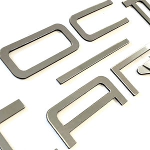 May include: Silver metal letters spelling out the word "Ford" in a modern font style.