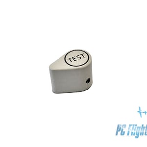 Puede incluir: Un interruptor de prueba de plástico blanco con un círculo negro y la palabra "TEST" impresa en él.