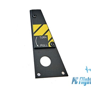 Może przedstawiać: Czarny trójkątny panel sterowania samolotem z żółto-czarną paskowaną etykietą ostrzegawczą. Etykieta zawiera napis "TURN" ze strzałką skierowaną w lewo i "PULL" poniżej strzałki.