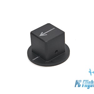 Op de afbeelding: Zwarte bedieningsknop met een pijltje op de bovenkant. De knop heeft een vierkante bovenkant en een cirkelvormige basis. De afbeelding staat tegen een witte achtergrond. De tekst "PC Flights" staat rechtsonder.