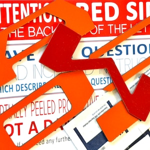 May include: Close-up of a set of orange and red paper cutouts with the text "ATTENTION IS THE BACK OF THE" and "QUESTIONS" visible. The cutouts are shaped like arrows and are arranged in a random pattern.