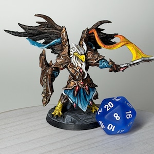 May include: A hand-painted miniature figurine of a warrior with eagle-like features, wearing bronze armor and holding a flaming weapon. The figure has large wings and is standing next to a blue, twenty-sided die. The figurine is on a black base.
