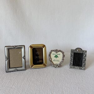 Peut inclure: Quatre petits cadres photo de styles variés. Les cadres sont argentés, dorés et argentés avec des détails décoratifs. Un cadre est en forme de cœur avec un motif floral. Les cadres sont vides, prêts pour les photos.