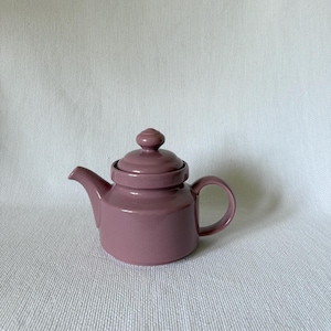Puede incluir: Pequeña tetera de cerámica de color malva con tapa a juego. La tetera tiene un pico curvo, un asa redondeada y un pomo en la tapa. La tetera está diseñada para preparar té y es adecuada para uso doméstico.