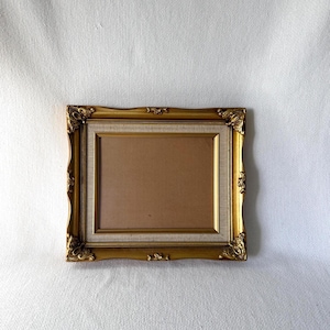 May include: A rectangular picture frame with an ornate gold finish featuring decorative corner detailing. The frame includes a textured off-white inner border and a plain brown backing insert, creating a layered appearance within the structure.