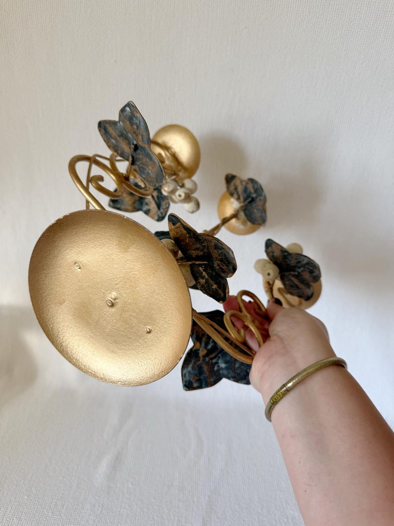 Puede incluir: Un candelabro de metal dorado con base redonda y detalles decorativos florales y de hojas. Las hojas son una mezcla de oro, azul y marr&oacute;n. El candelabro tiene un dise&ntilde;o caprichoso y art&iacute;stico.