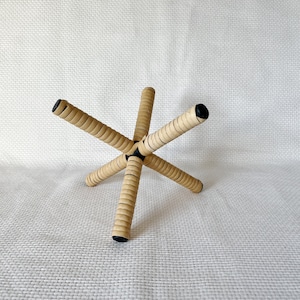Può includere: Un supporto in legno con cinque bracci, ognuno con una punta nera. Il supporto è in legno intrecciato e ha una forma a stella.