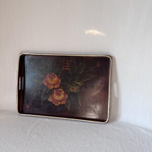Può includere: Un vassoio da portata in legno vintage con un bordo argentato. Il vassoio presenta un design dipinto a mano con rose gialle e foglie verdi su uno sfondo marrone scuro.