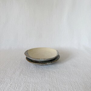 May include: Two small ceramic bowls stacked on top of each other. The top bowl is white with a light gray rim. The bottom bowl is a darker gray with a white rim.