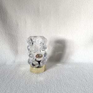 Op de afbeelding: Een doorzichtige glazen flesstopper met een bubbelontwerp en een goudkleurige basis. De stopper is cilindrisch en heeft een reeks heldere, afgeronde bellen. De basis heeft een glanzende goudkleur.