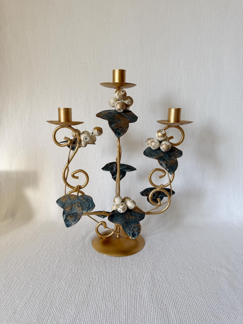 Vintage gold metal candelabra with green leaves and cream wooden berries, three-arm candle holder, romantic Italian-style home decor.