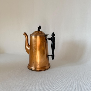 May include: A vintage copper coffee pot with a black handle and lid finial. The pot has a spout and a rounded body. The copper has a warm, reddish-brown hue, and the handle and finial are black.