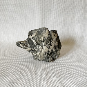 Può includere: Un piccolo vaso in ceramica bianco e nero con una superficie ruvida e testurizzata. Il vaso ha la forma di una roccia o di una piccola scultura astratta.