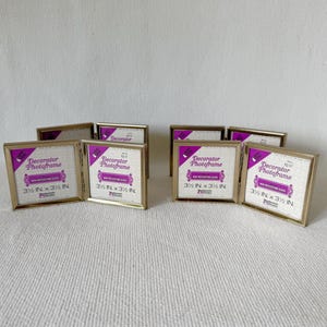 Puede incluir: Una colección de marcos de fotos de metal dorado, cada uno con un interior blanco y una etiqueta que dice "Decorator Photoframe 3 ½ IN x 3 ½ IN." Los marcos están dispuestos sobre una superficie blanca texturizada. (Aprox. 8,9 cm x 8,9 cm).