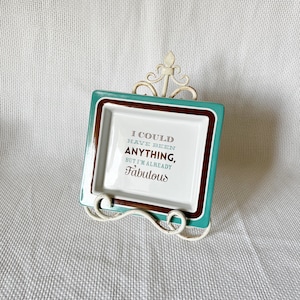 May include: A white ceramic dish with a brown and teal border. The dish has the text "I could have been anything, but I'm already fabulous" printed on it.