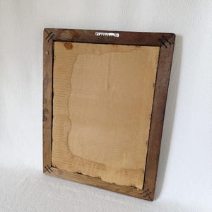 Puede incluir: Parte trasera de un marco de fotos rectangular de madera con respaldo de cart&oacute;n. El marco es de color marr&oacute;n oscuro y tiene un colgador de sierra. El respaldo de cart&oacute;n tiene manchas de agua y est&aacute; parcialmente rasgado.