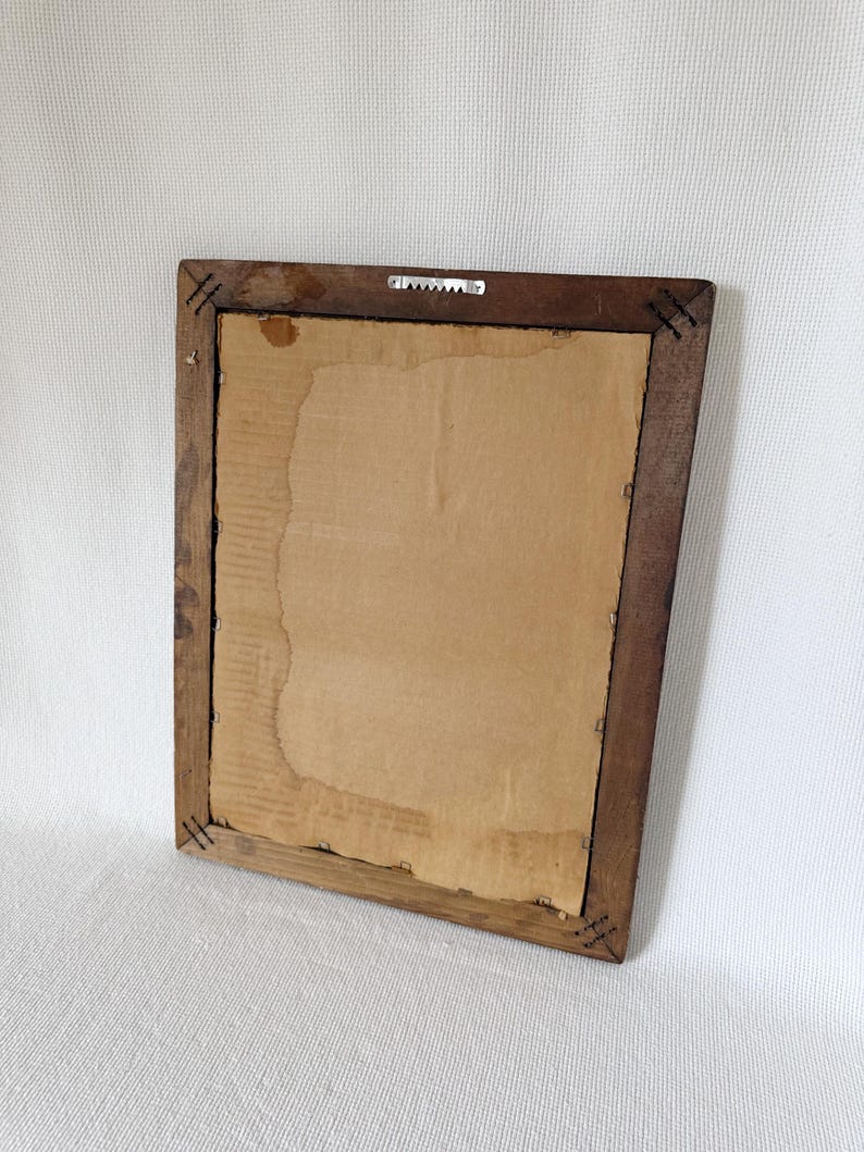 Puede incluir: Parte trasera de un marco de fotos rectangular de madera con respaldo de cart&oacute;n. El marco es de color marr&oacute;n oscuro y tiene un colgador de sierra. El respaldo de cart&oacute;n tiene manchas de agua y est&aacute; parcialmente rasgado.