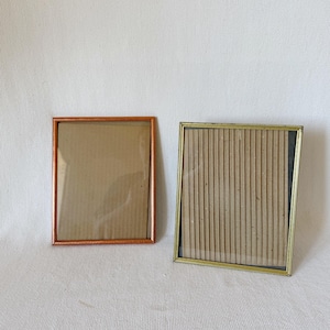 May include: Two picture frames, one with a copper-colored frame and one with a gold-colored frame. Both frames are empty and have a cardboard backing.