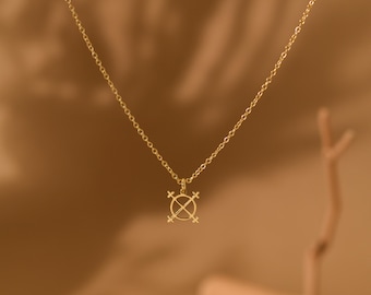 May include: A gold-colored necklace with a pendant featuring a cross-like design within a circle. The chain is delicate, and the pendant hangs in the center. The background is a warm, neutral tone, highlighting the jewelry.