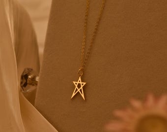 May include: A gold-toned necklace featuring a delicate chain and a five-pointed star pendant. The star design is composed of thin, interconnected lines forming a geometric shape. The necklace is displayed on a neutral-colored stand.