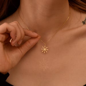 Op de afbeelding: Een delicate goudkleurige ketting met een hanger met een sterrenpatroon. De ketting wordt getoond tegen een huidskleurige achtergrond, waardoor de ingewikkelde details en elegante eenvoud van de sieraden worden benadrukt. De ketting is fijn en de hanger is klein.