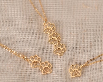 May include: Three gold necklaces with paw print pendants. The pendants are engraved with the letters "B", "E", and "N".