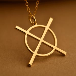 Puede incluir: Un collar con colgante dorado con un diseño geométrico. El colgante tiene un círculo con dos líneas que se cruzan, creando cuatro secciones iguales. La cadena también es dorada y delicada, adecuada para el uso diario.
