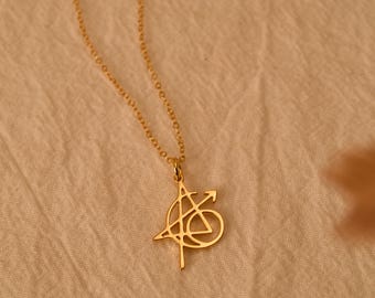Pode incluir: Um colar de tom dourado com uma corrente fina e um pingente em forma do logotipo dos Vingadores. O pingente é uma letra A estilizada dentro de um círculo, com uma seta estendendo-se para o lado direito, tudo com acabamento dourado.
