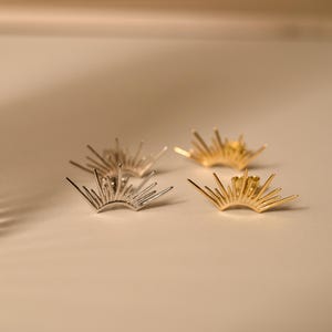 May include: Four pairs of sunburst-shaped stud earrings. Two pairs are silver-toned, and two are gold-toned. The earrings have a spiky, radial design, with each earring featuring multiple thin, radiating lines. The earrings are displayed on a neutral background.