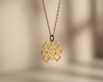 May include: A gold pendant necklace with a sun-shaped charm. The pendant has a geometric design with a smiling face. The chain is fine and gold, set against a neutral backdrop. The necklace is a piece of jewellery.