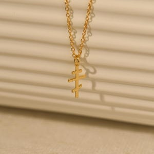 May include: A gold-colored necklace with a pendant in the shape of a cross. The cross has three horizontal bars. The chain is delicate and the pendant is small. The necklace is displayed against a neutral background.