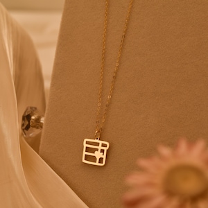 May include: A gold-toned necklace featuring a delicate chain and a square-shaped pendant with a cutout design resembling a gift box tied with a ribbon, including a small heart-shaped detail centered on the front of the square pendant.
