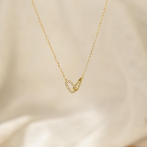 May include: A delicate gold necklace featuring two interlocking loops. One loop is adorned with small, clear gemstones, adding a touch of sparkle. The necklace hangs on a fine chain, creating a minimalist and elegant design.