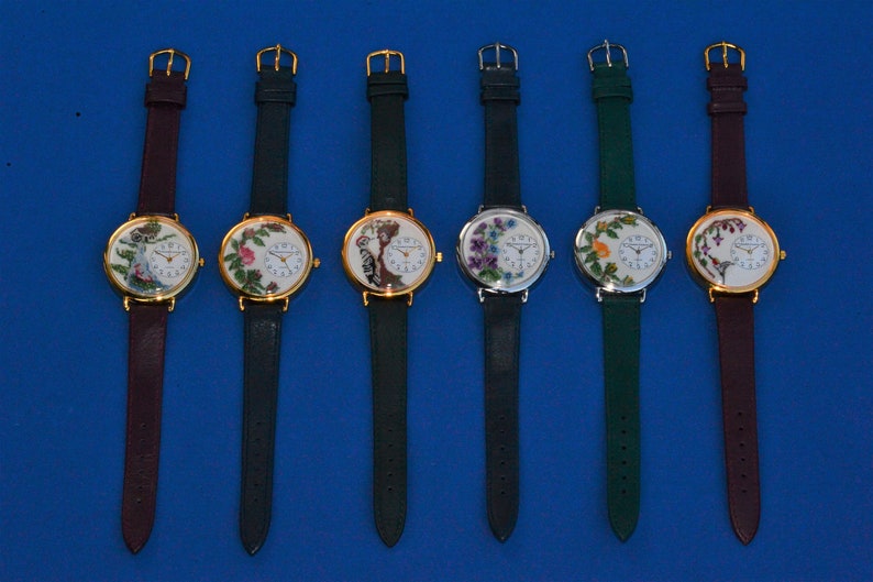 May include: Six wristwatches with different floral embroidery designs on the face. The watches have gold, silver, and white face plates with black hands. The bands are either dark green or burgundy.