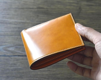 May include: A bi-fold wallet in a warm, amber-toned leather. The wallet has a glossy finish and is stitched with white thread around the edges. The interior is a contrasting orange colour.