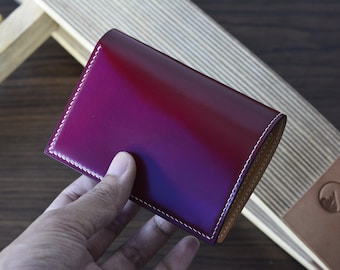 May include: A burgundy leather wallet with white stitching. The wallet is folded in half and held in a hand.