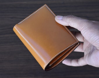 May include: A brown leather wallet with white stitching. The wallet is folded in half and is being held in a hand.