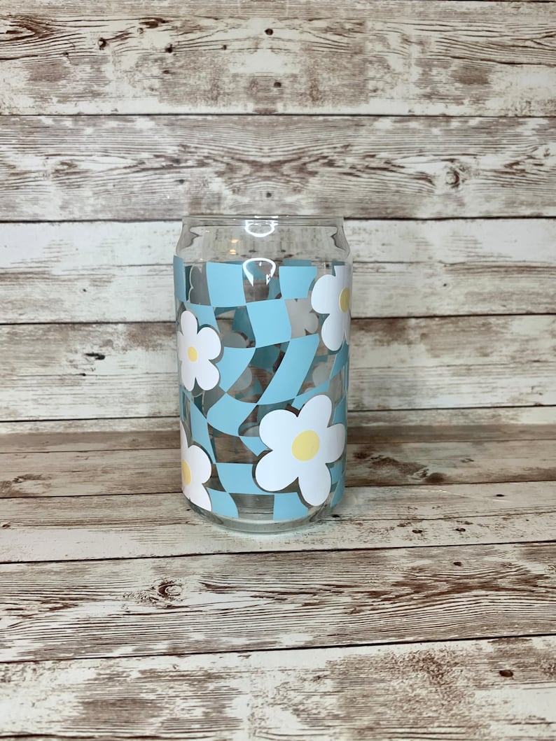 May include: A glass can with a blue and white checkered pattern and white daisies with yellow centres.