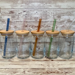 May include: Five glass drinking jars with wooden lids and glass straws. The straws are blue, pink, orange, green, and clear.