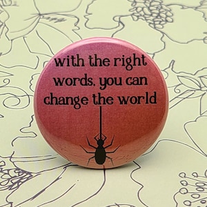 Könnte beinhalten: Ein roter Knopf mit dem Text "with the right words, you can change the world" und einer schwarzen Silhouette einer Spinne.