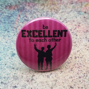 May include: A circular, magenta badge featuring the words "be EXCELLENT to each other" in black. Two black silhouettes of people with raised arms are below the text. The badge has a striped pattern.