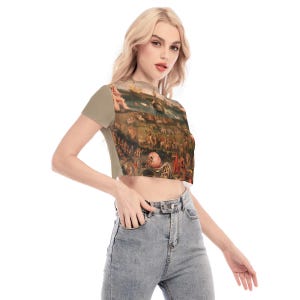 Puede incluir: Una camiseta corta con estampado de pintura renacentista. La camiseta tiene mangas cortas y un color beige en las mangas y la espalda. La parte delantera de la camiseta muestra una obra de arte detallada y multicolor.