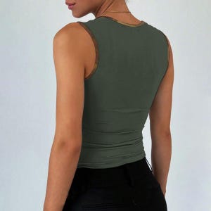 May include: Olive green vest top with a scoop neck and brown trim. The sleeveless top is form-fitting and paired with black trousers. The top is made of a smooth, stretchy material.