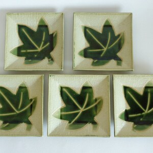 May include: Set of five square ceramic plates with a green leaf design. The plates are a light green colour with a white background. Each plate features a stylised green leaf with a gold outline.
