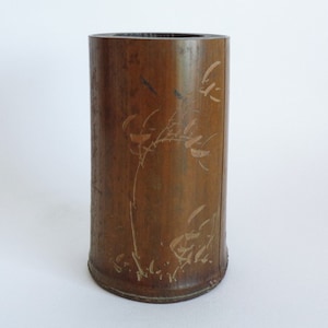 Puede incluir: Un jarrón de bambú marrón con un diseño decorativo de ramas y hojas estilizadas en un color marrón más claro.